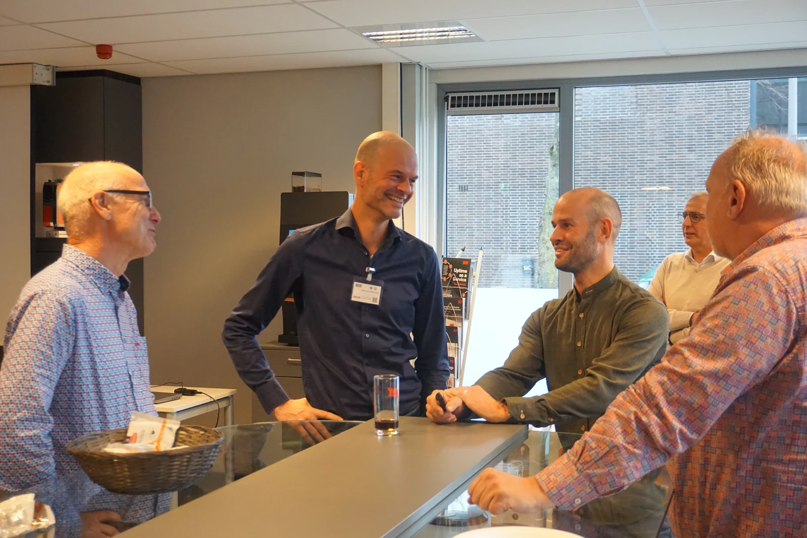 Vijf mensen in een ontspannen gesprek rond een hoge tafel